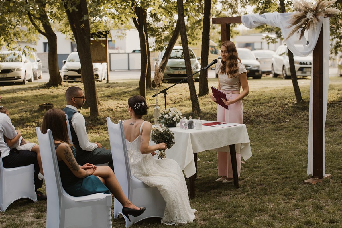 Szabadtéri esküvői szertartás: a pár a vendégek előtt áll, Nimsz Zsuzsanna vezeti a ceremóniát